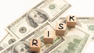 Wooden letter blocks spelling RISK sit on scattered US $100 bills, illustrating financial risk