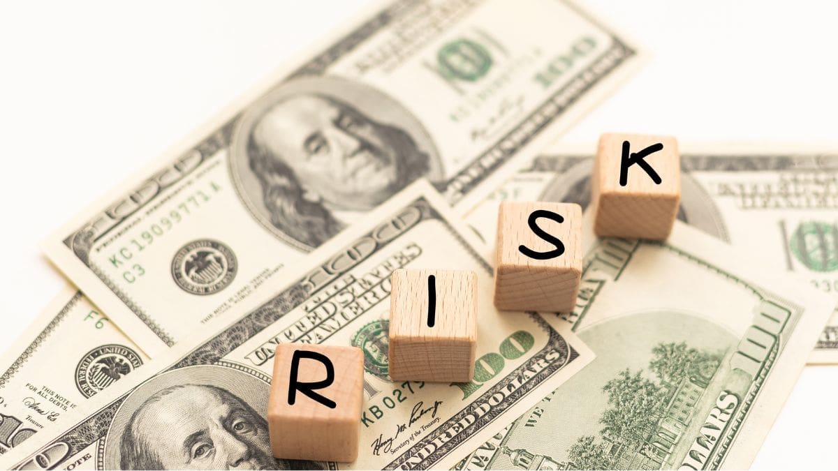 Wooden letter blocks spelling RISK sit on scattered US $100 bills, illustrating financial risk