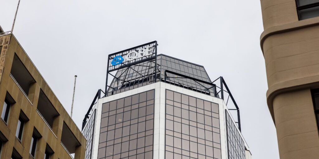 Modern glass office building seen from below with a blue company logo sign atop.