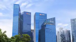 Allianz strikes S$2.7bn deal for HSBC Life Singapore Blue glass skyscrapers in a financial district with bank logos DBS, HSBC and Standard Chartered visible on the towers, against a blue sky with palm trees in the foreground