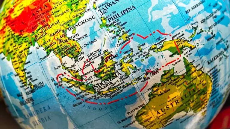 Close-up of a world globe focusing on Southeast Asia and Australia, with red travel routes drawn over the map.
