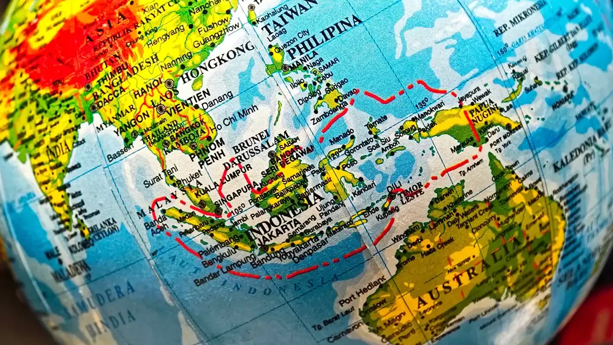 Close-up of a world globe focusing on Southeast Asia and Australia, with red travel routes drawn over the map.
