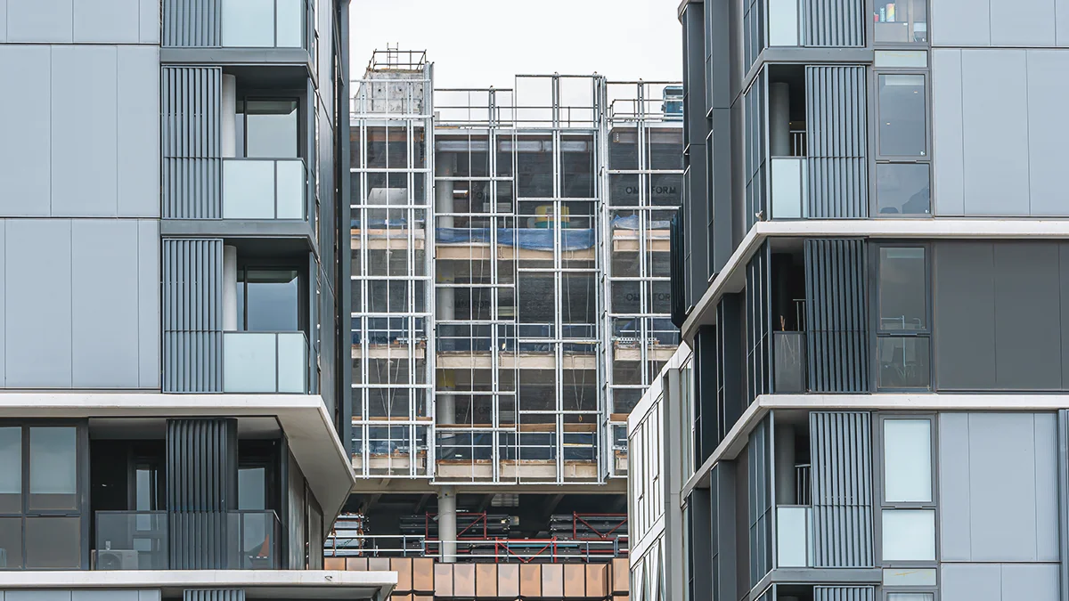 Modern glass apartment blocks with a construction site in between, showing scaffolding and exposed framework in the center still under build.