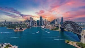 Sydney skyline at sunset with the Opera House and Harbour Bridge over the blue harbor sea, boats visible on the water