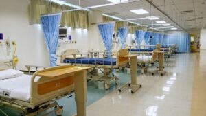 BNM plans independent oversight framework for MediAsas Empty hospital ward with row of beds separated by blue curtains, bright lights, and medical equipment nearby.