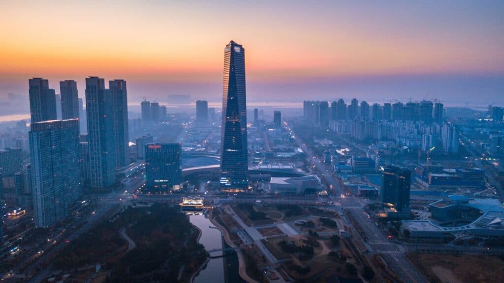 Aerial view of a modern city skyline at sunset with a tall central skyscraper and a river in the distance,