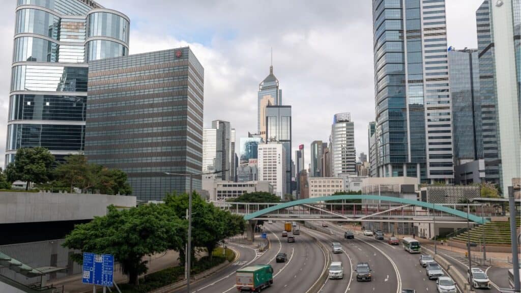 City skyline with tall glass skyscrapers and a curved road bridge over a multi-lane highway in the foreground.