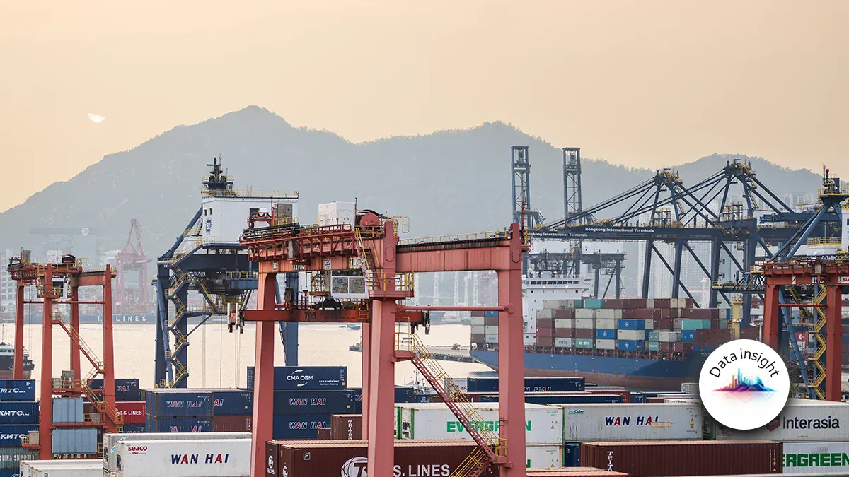 Port scene at sunset with red gantry cranes, stacked shipping containers, and a container ship; mountains in the distance.
