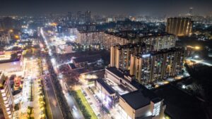 Night aerial view of a modern city with illuminated streets and high-rise residential blocks on both sides of a main road at night.