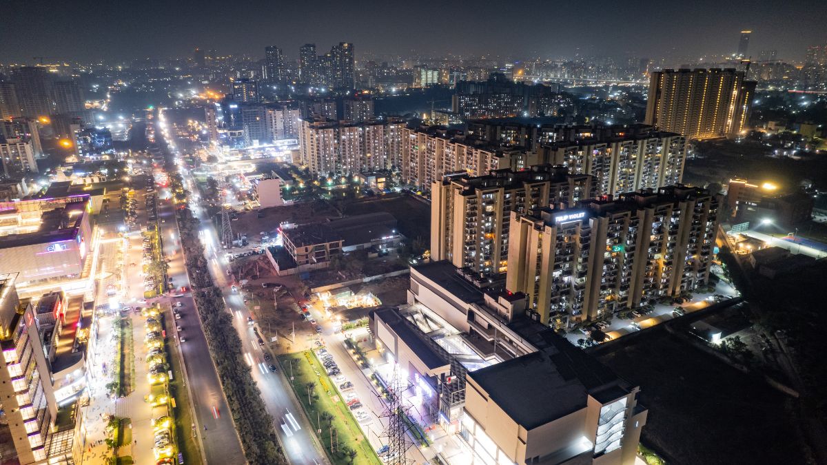 Night aerial view of a modern city with illuminated streets and high-rise residential blocks on both sides of a main road at night.