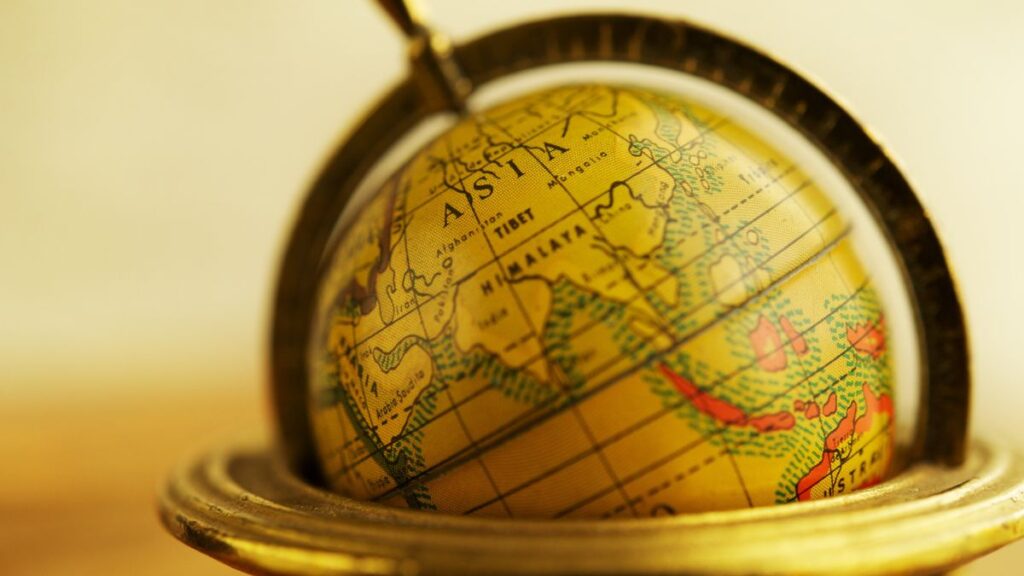 Golden globe resting inside a brass stand with over-ear headphones draped over it, bathed in warm light, suggesting global listening or travel.