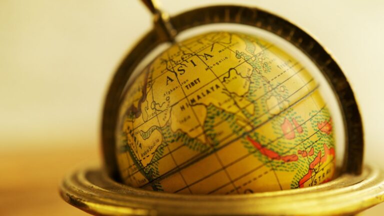 Golden globe resting inside a brass stand with over-ear headphones draped over it, bathed in warm light, suggesting global listening or travel.