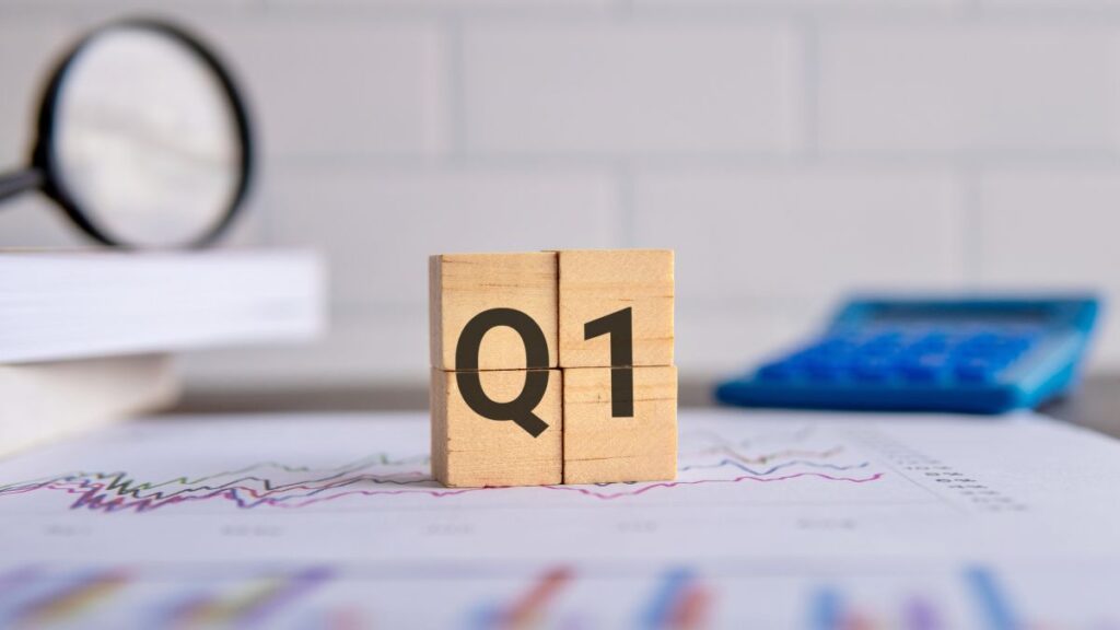 Wooden blocks spell out Q1, symbolizing the first quarter of the year on a desk with graphs and a calculator in the background