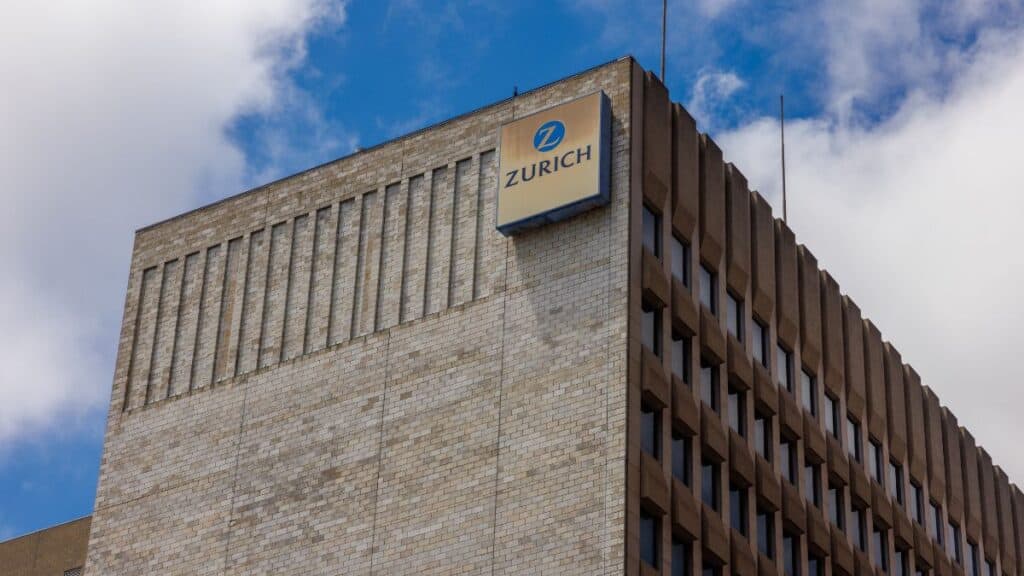Brick office building with a Zurich logo sign on the roof against a blue sky.