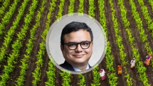 Aerial view of a farm with evenly spaced green crop rows and a circular portrait of a man wearing glasses centered over the field.