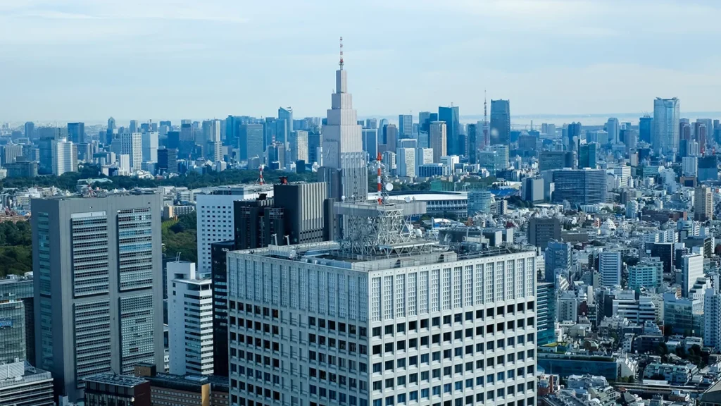 Aerial view of a dense city skyline with many high-rise buildings and a prominent stepped central tower against a blue sky.
