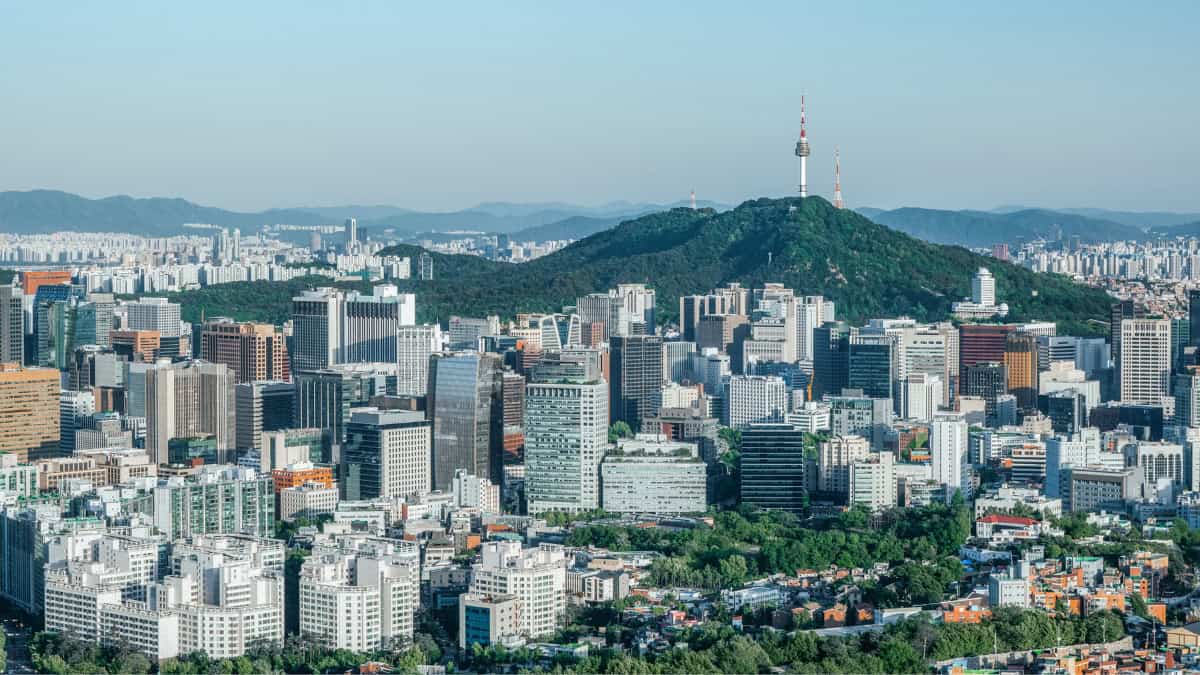 Dense city skyline with a green hill and a tall communications tower rising above the hills in the distance.