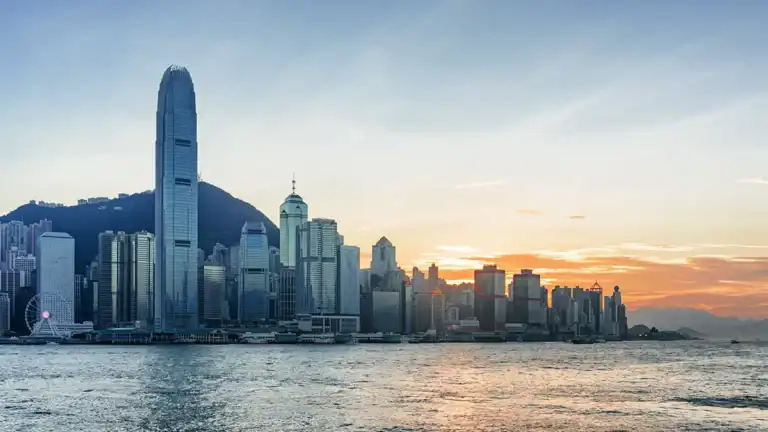 Hong Kong skyline at sunset with Victoria Harbour, featuring the IFC tower and a dense row of skyscrapers along the water.