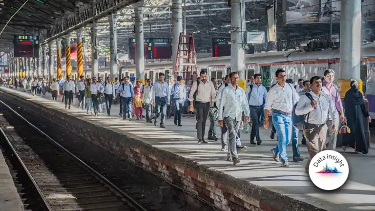 Crowded railway platform with hundreds of commuters walking beside a stationary train under a shelter on a busy station.