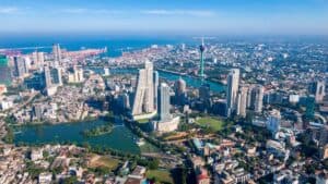 Aerial view of a modern city with high-rise buildings, winding rivers, and a distant harbor under a clear blue sky.",