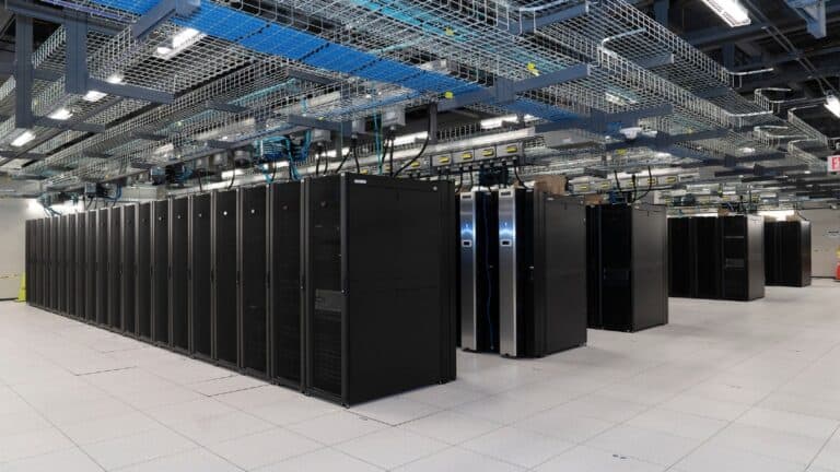 Data center with a long row of black server racks and overhead cable trays.