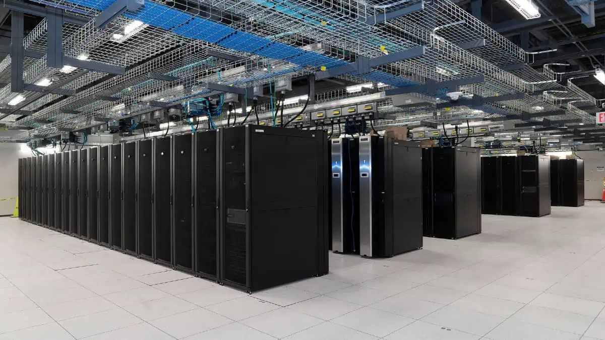 Data center with a long row of black server racks and overhead cable trays.