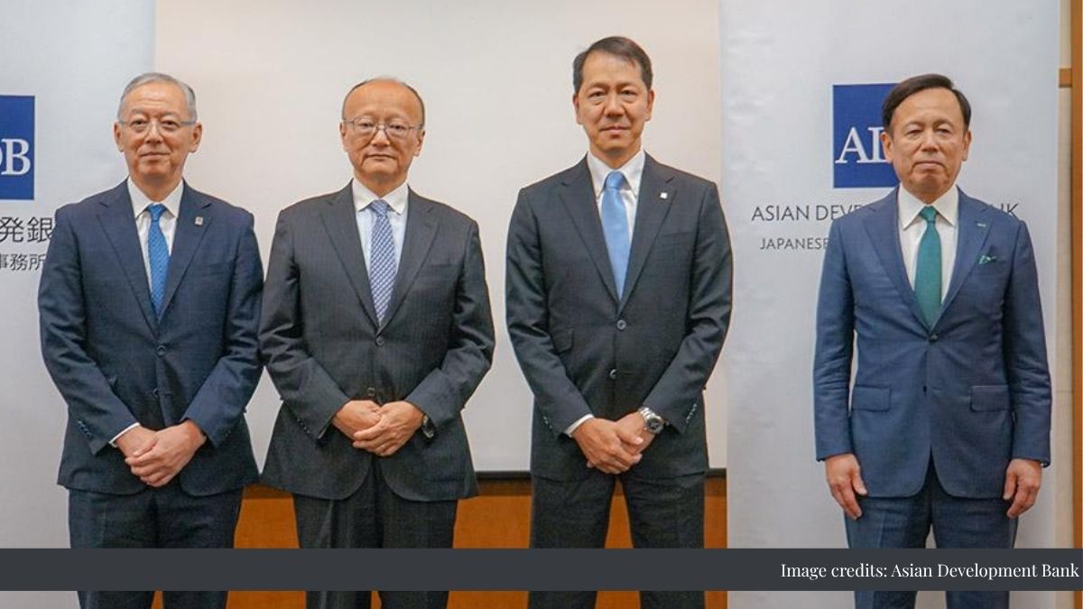 Four men in dark suits pose for a photo at a conference, with Asian Development Bank banners in the background.