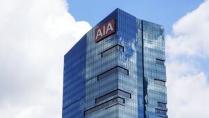 Blue glass skyscraper with an AIA sign on the upper corner against a partly cloudy sky.
