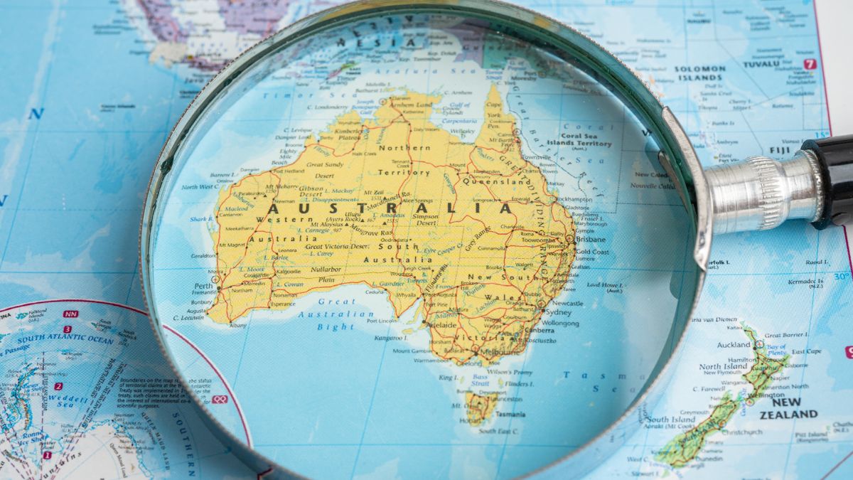 Magnifying glass over a map of Australia, emphasizing the continent and surrounding waters.