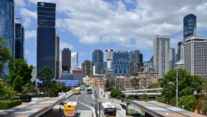 City skyline with tall glass skyscrapers, a multi-lane road, and buses in the foreground.