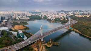 Bajaj Finserv wins board approval to enter India's reinsurance market Aerial view of a city with a prominent cable-stayed bridge over a wide river lake surrounded by buildings and green spaces, taken from above the skyline.