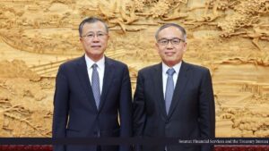 Two Asian men in dark suits pose side by side in front of a large golden carved wall.