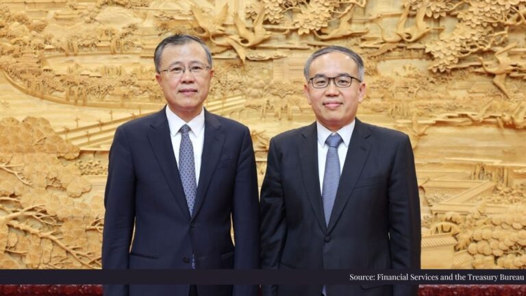 Two Asian men in dark suits pose side by side in front of a large golden carved wall.
