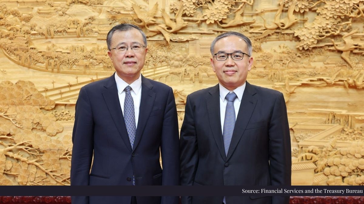 Two Asian men in dark suits pose side by side in front of a large golden carved wall.