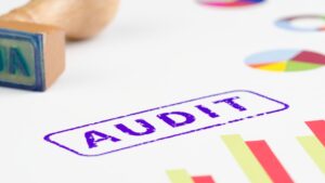Purple 'AUDIT' stamp on a white surface with colorful charts in the background.