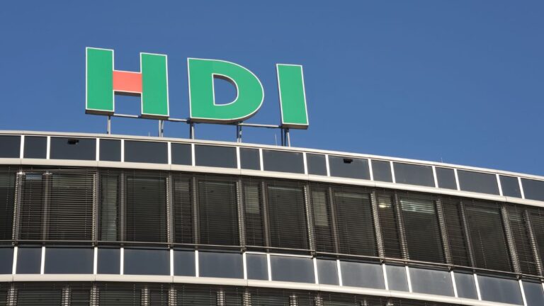 Office building façade with a large green HDI sign on the roof against a clear blue sky.