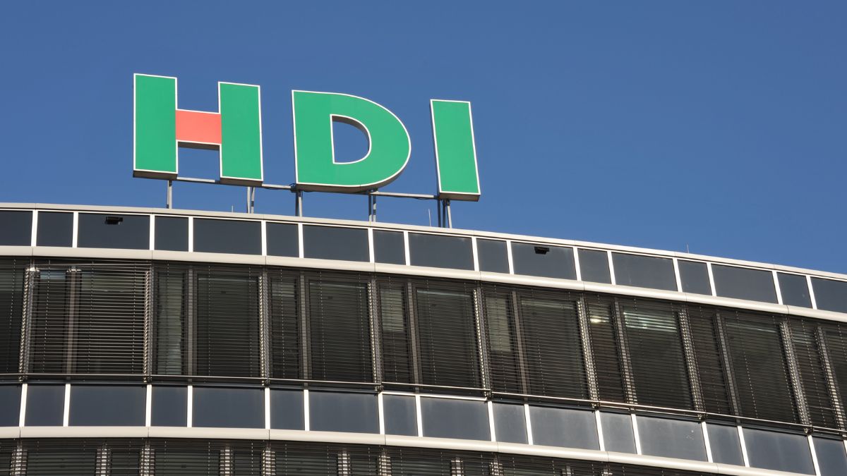 Office building façade with a large green HDI sign on the roof against a clear blue sky.