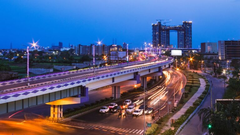 Urban highway in India with city skyline and ongoing construction at dusk.