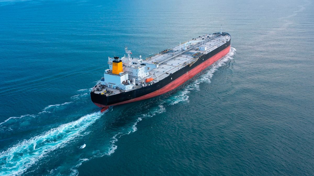 Aerial view of a large black-and-red oil tanker sailing through calm blue sea with a yellow smokestack and white superstructure at the stern.