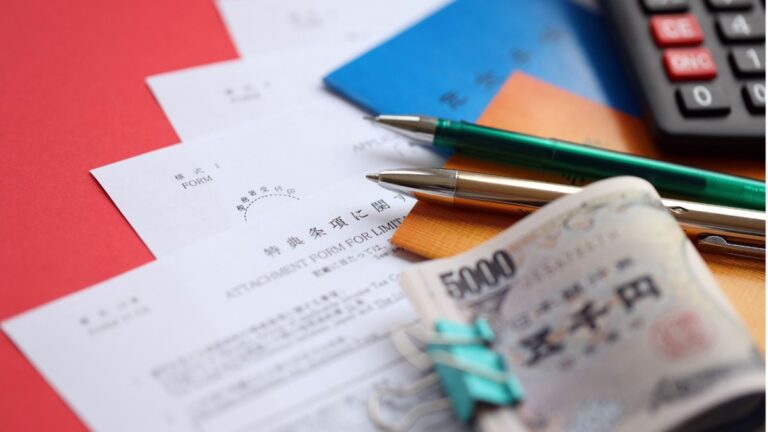 Close-up of accounting forms, a 5,000 yen banknote, pens, and a calculator on a red desk.