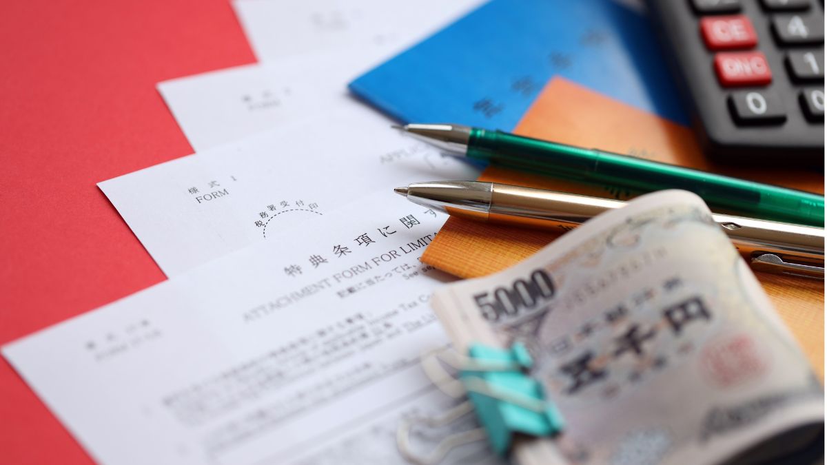 Close-up of accounting forms, a 5,000 yen banknote, pens, and a calculator on a red desk.