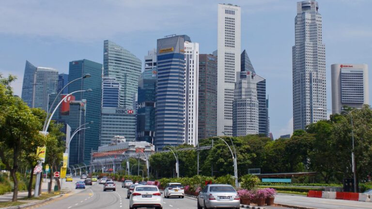 City skyline with tall modern skyscrapers and a busy road lined with trees in the foreground.