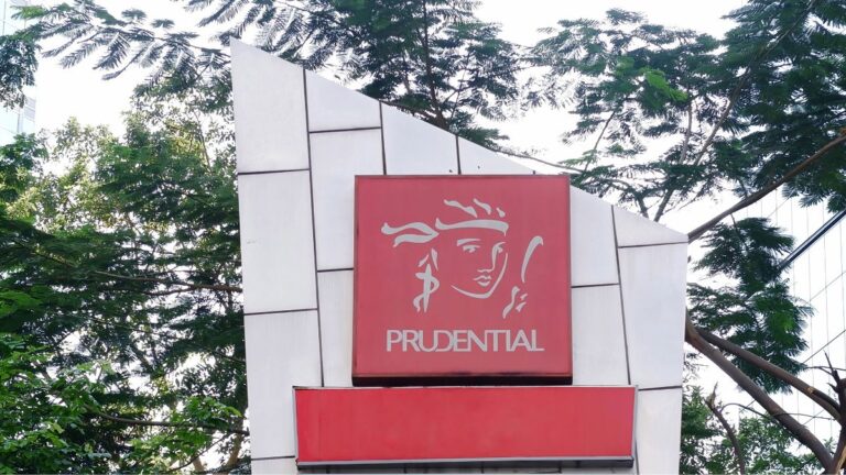 Prudential red square sign with white Liberty head logo on a white geometric facade, trees behind.