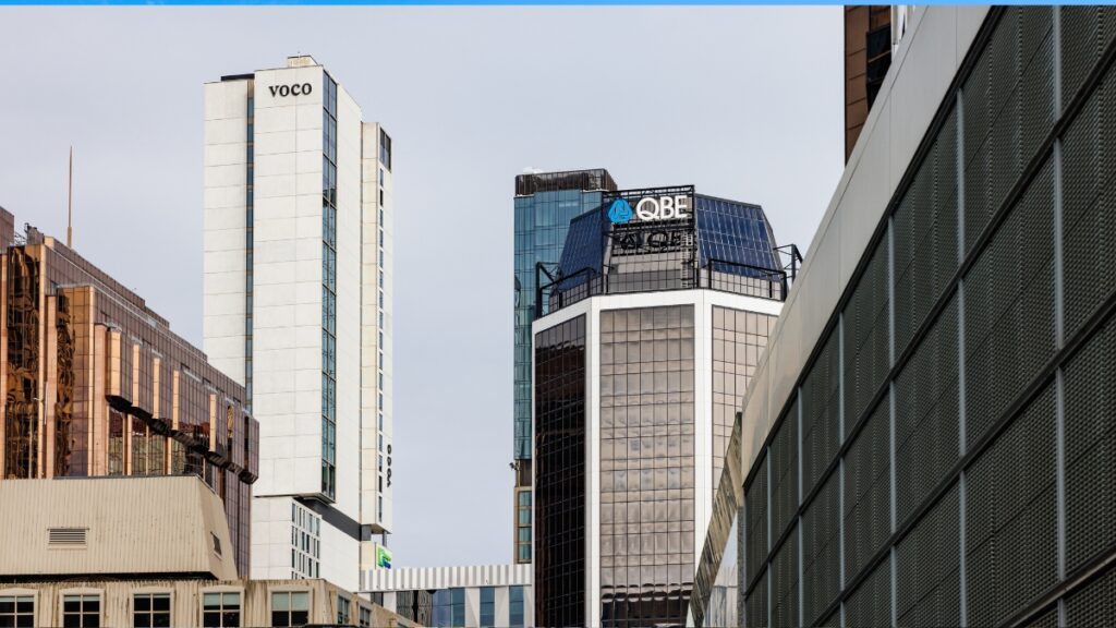 Skyline of modern office towers with VOCO and QBE logos against a clear blue sky.