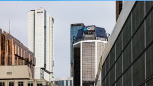 QBE Australia Pacific MD Elliot Hill to exit at end of August Skyline of modern office towers with VOCO and QBE logos against a clear blue sky.