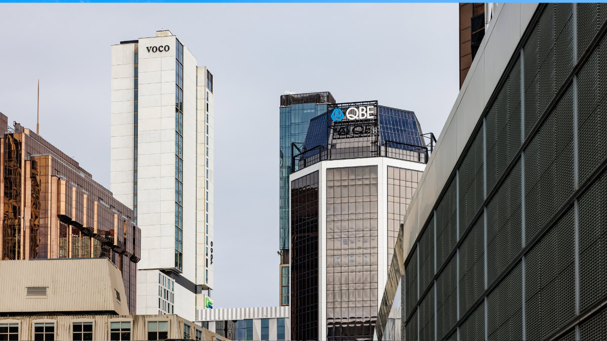 Skyline of modern office towers with VOCO and QBE logos against a clear blue sky.