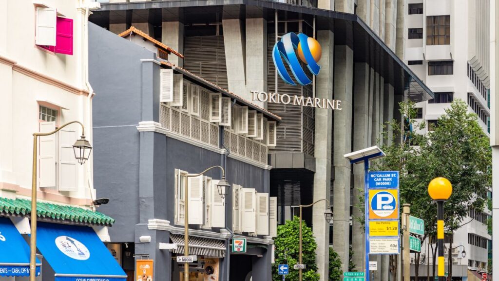 Tokyo Marine logo on a tall modern building with a busy street of shopfronts and street lamps in front.