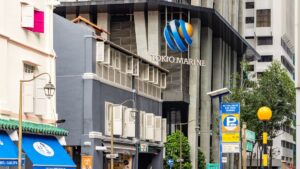 Tokyo Marine logo on a tall modern building with a busy street of shopfronts and street lamps in front.