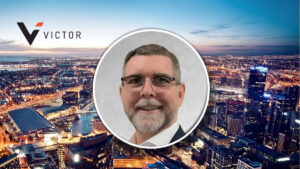 Smiling man in glasses in a circular frame centered over a nighttime city skyline with the Victor logo on the left.
