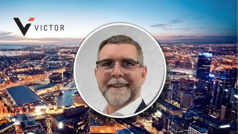 Smiling man in glasses in a circular frame centered over a nighttime city skyline with the Victor logo on the left.